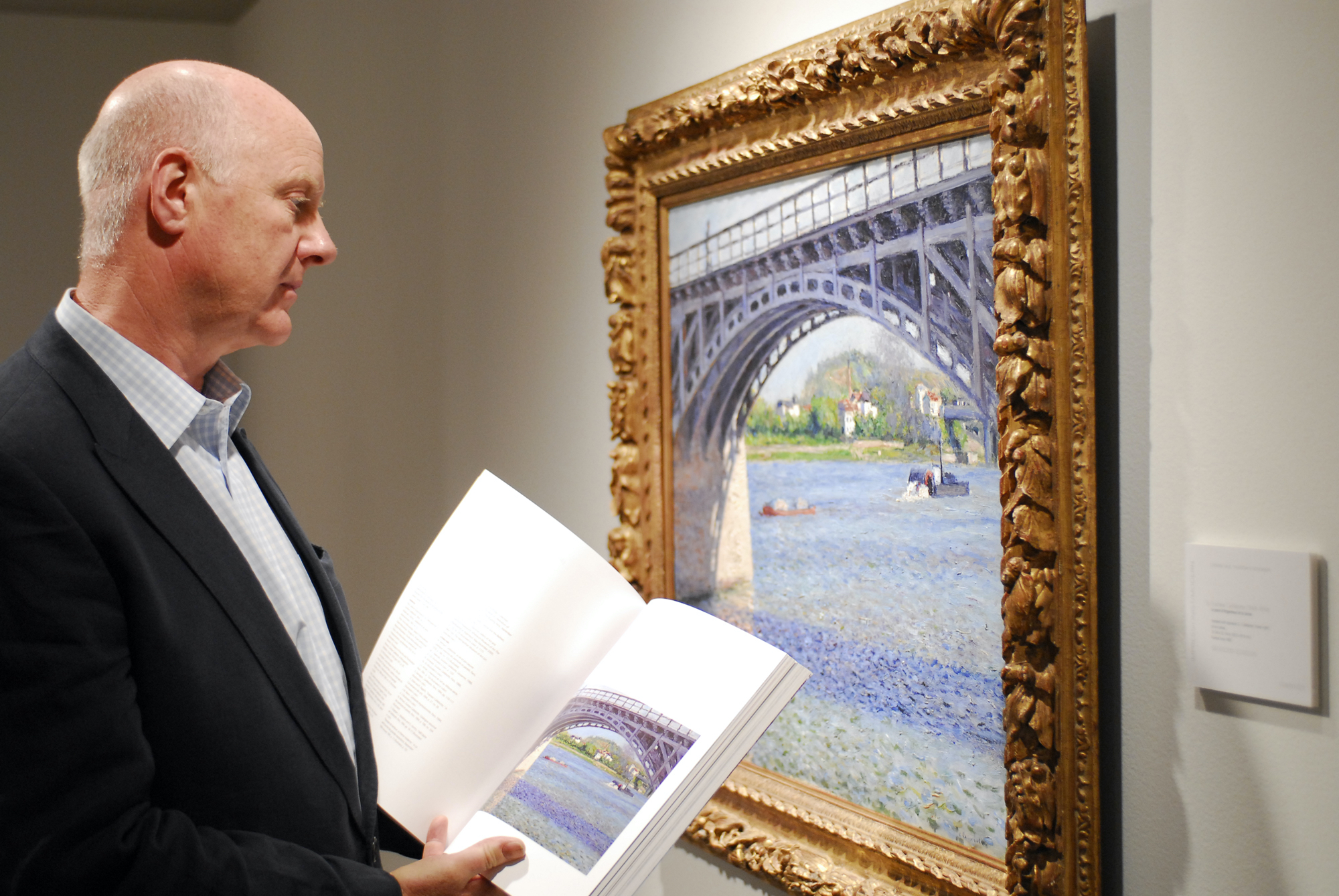 Ray Waterhouse viewing a waterscape painting by Gustave Caillebotte at Christie's auction house while holding an open catalog
