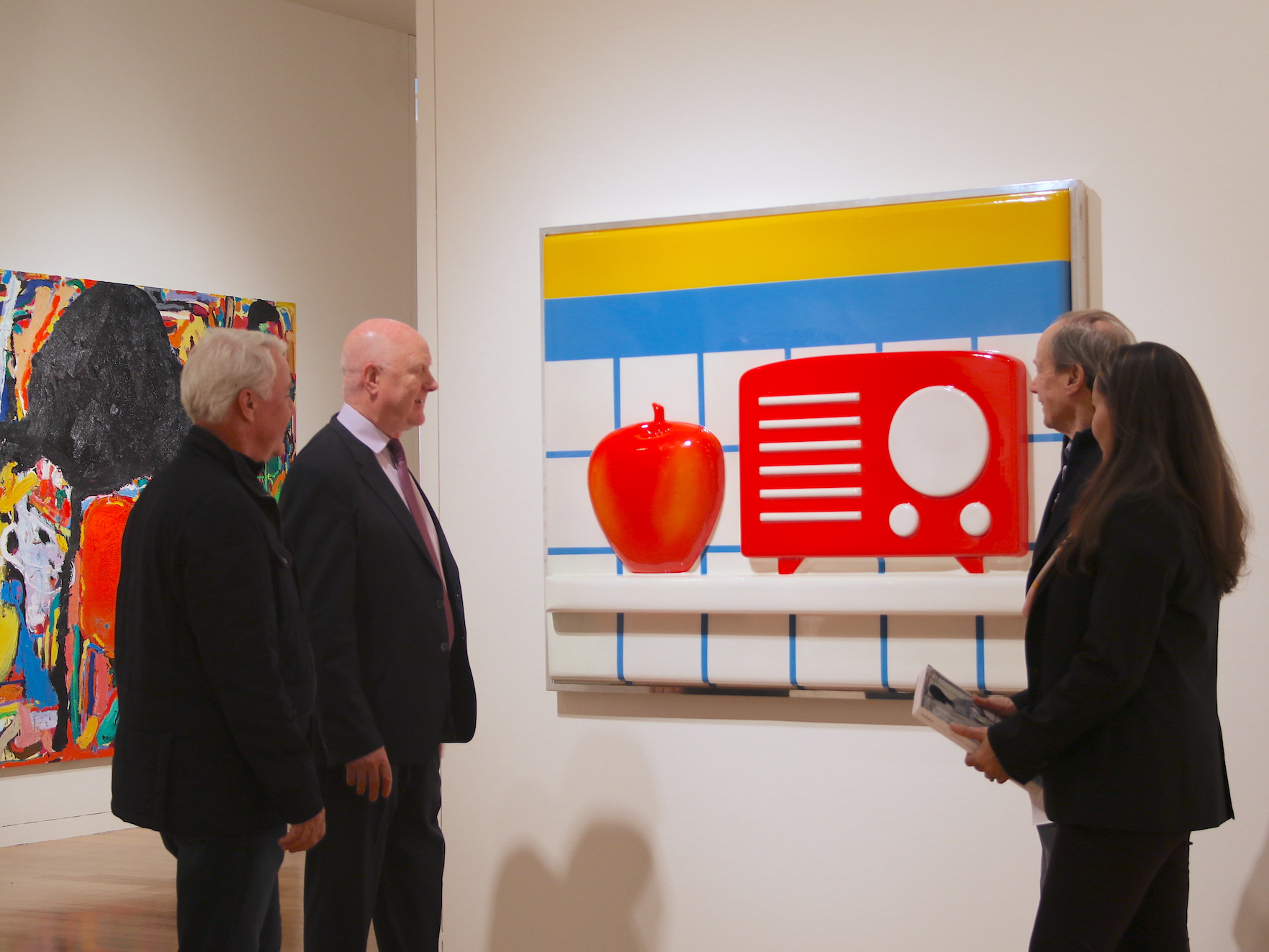 Ray, Sandra Safta Waterhouse, and clients in front of 2D artwork with large red apple and radio against tile background.