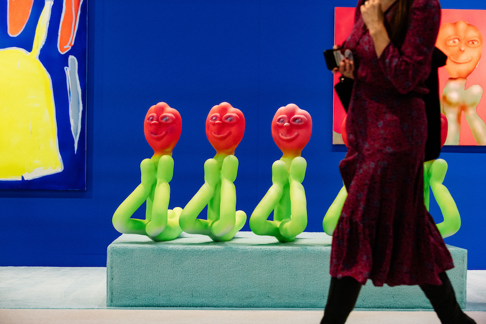 A woman walks in front of a sculptural artwork with abstract flowers with faces at the 2020 Armory Fair