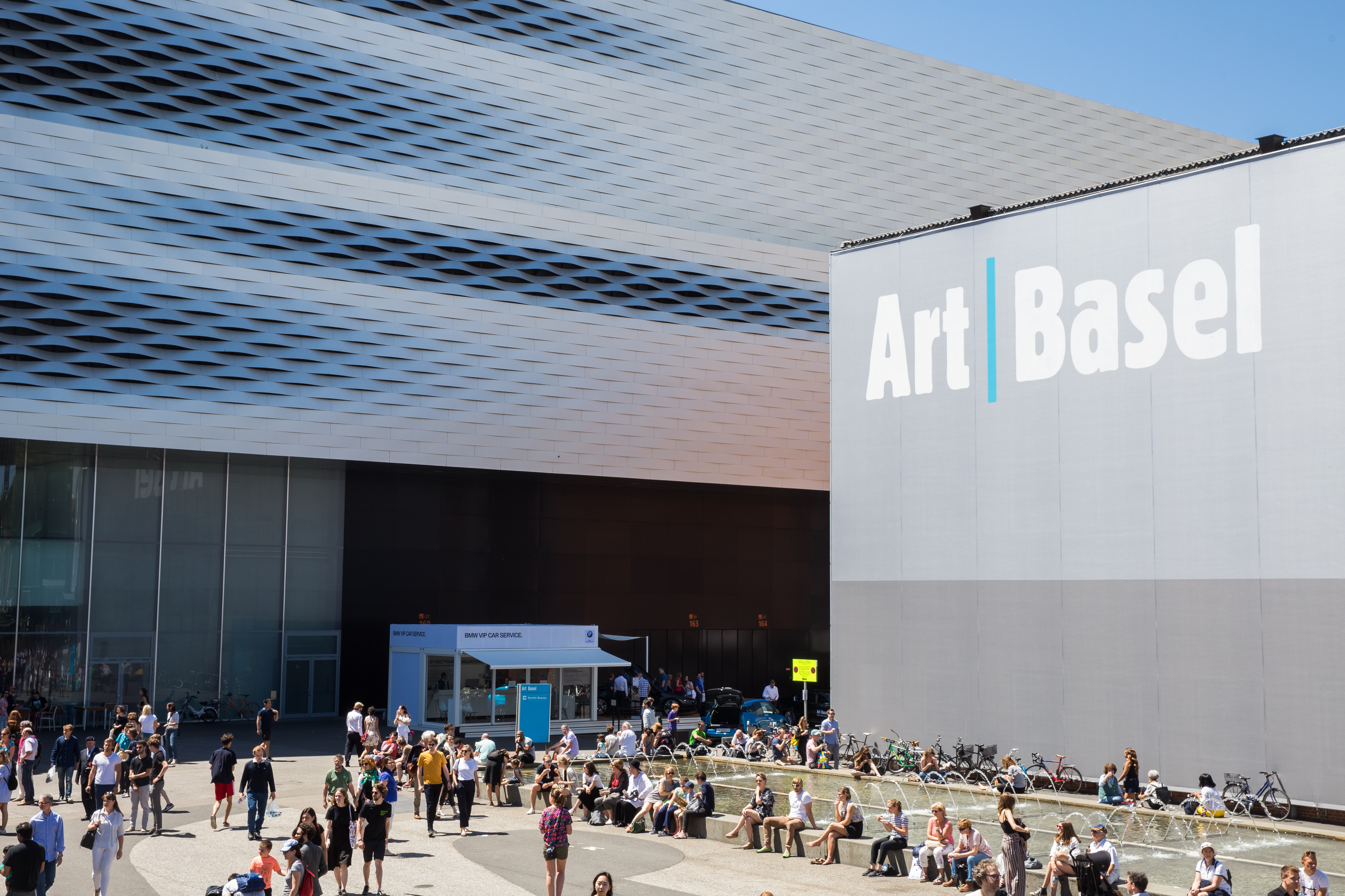 A crowd sits outside in front of a fountain at the 2019 Art Basel art fair