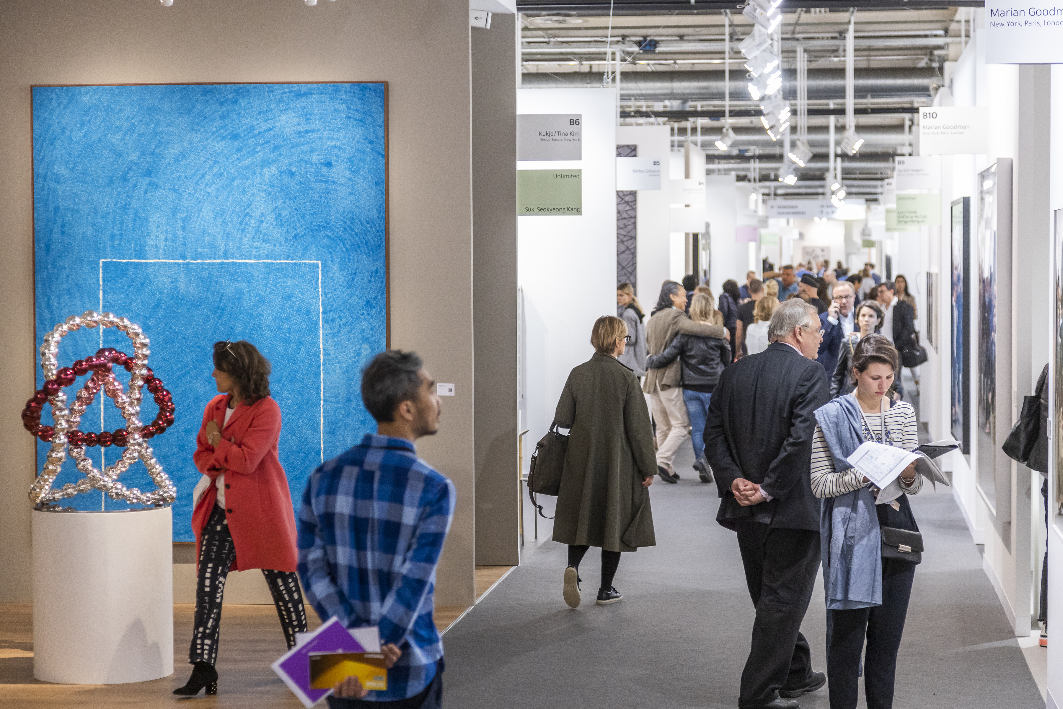 Art enthusiasts walk the art booths including a shiny beaded sculpture and large blue painting at Art Basel (2019).