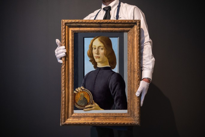 A man wearing white gloves holds Sandro Botticelli’s "Portrait of a Young Man Holding a Roundel"
