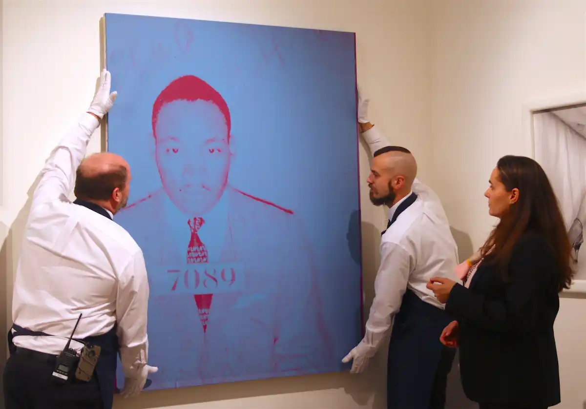 Two men hold a large fine art print of MLK's mugshot while Sandra Waterhouse oversees