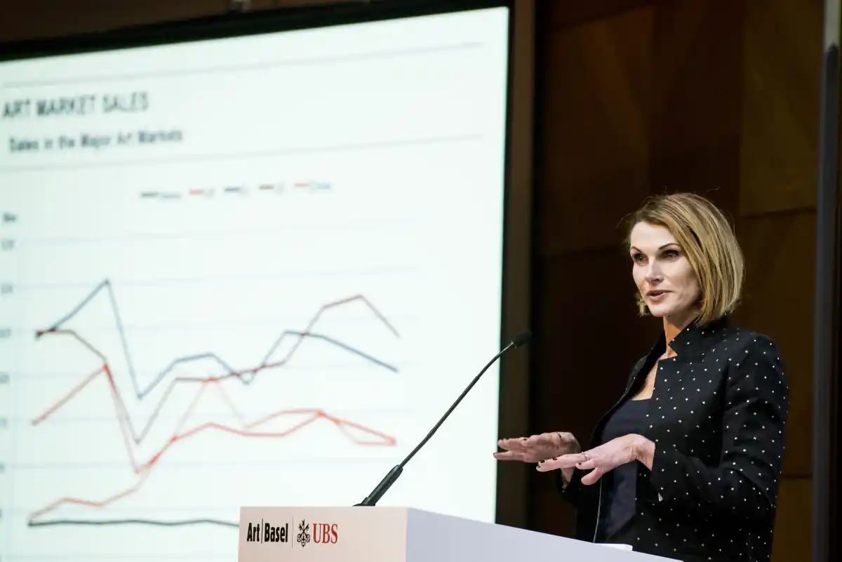 Dr. Clare McAndrew, an investment analyst talking about the 2022 fine art market at a podium with slideshow behind her.